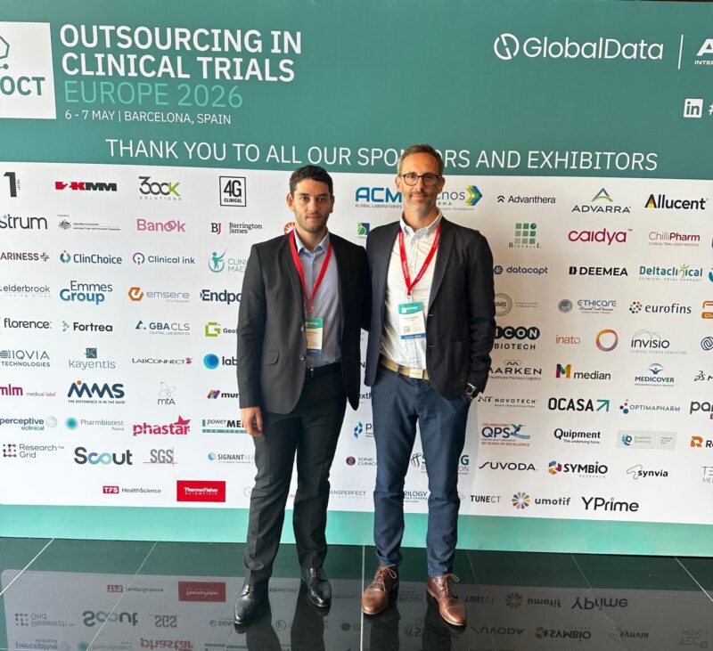Sami El Husseini et Frédéric Valenti à OCT Europe 2026 à Barcelone, devant le mur des sponsors et exposants.